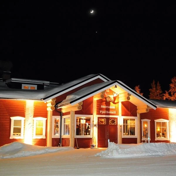 Storsätra fjällhotell en vinterkväll med upplyst fasad och månskära på himlen