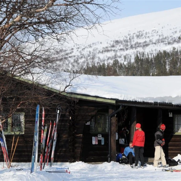 Sjöstugan i vinterskrud med längdskidor lutade mot väggen och fjället bakom